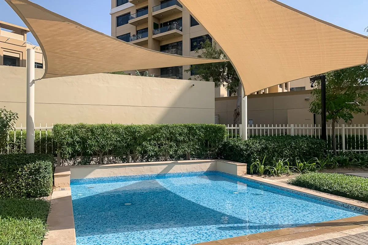 Una piscina al aire libre está bajo grandes toldos de sombra, junto a vegetación.