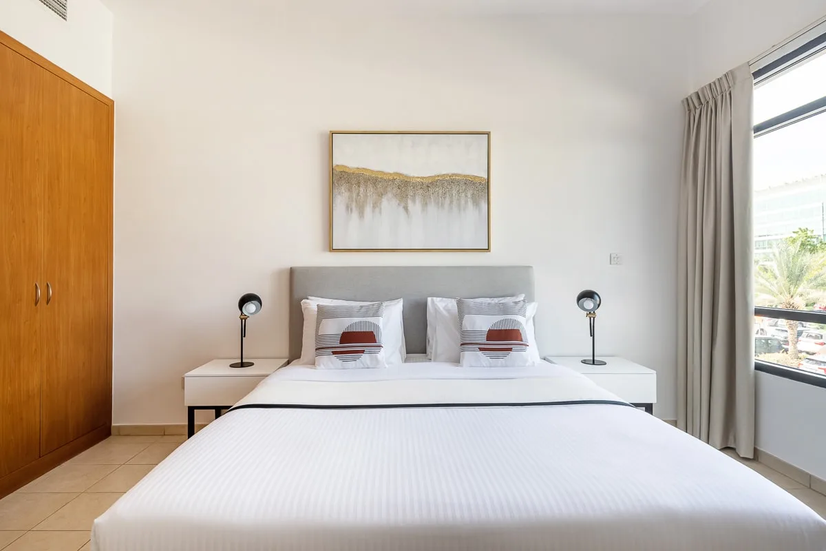 Un dormitorio luminoso con una cama tendida y una ventana grande.