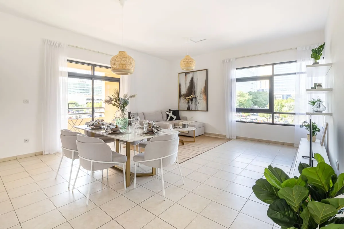 Una luminosa zona de comedor y estar con mesa, asientos y grandes ventanas.