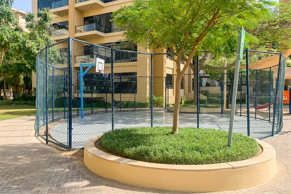 Una cancha de baloncesto al aire libre está junto a un jardín y un edificio de apartamentos.
