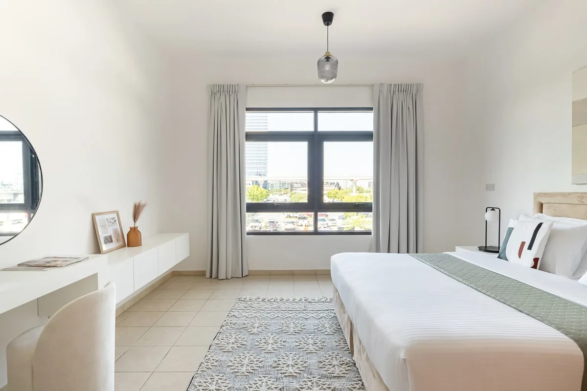 Un dormitorio luminoso con una ventana grande, una cama y una alfombra estampada.