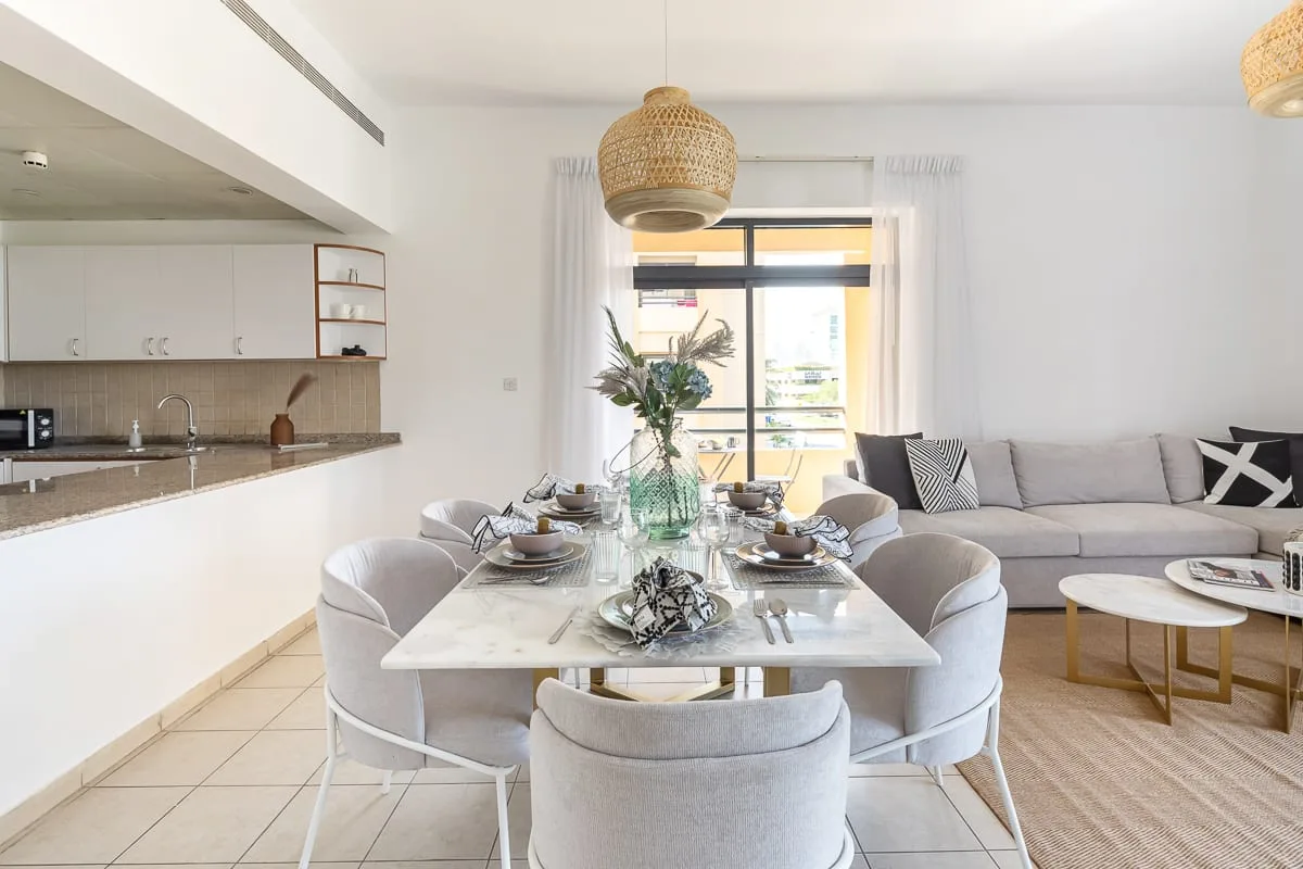 Una luminosa zona de comedor y estar con la mesa puesta y asientos junto a la ventana.