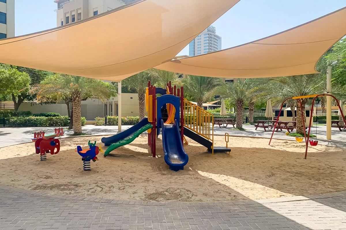 Un parque infantil de arena con juegos coloridos está bajo grandes toldos.