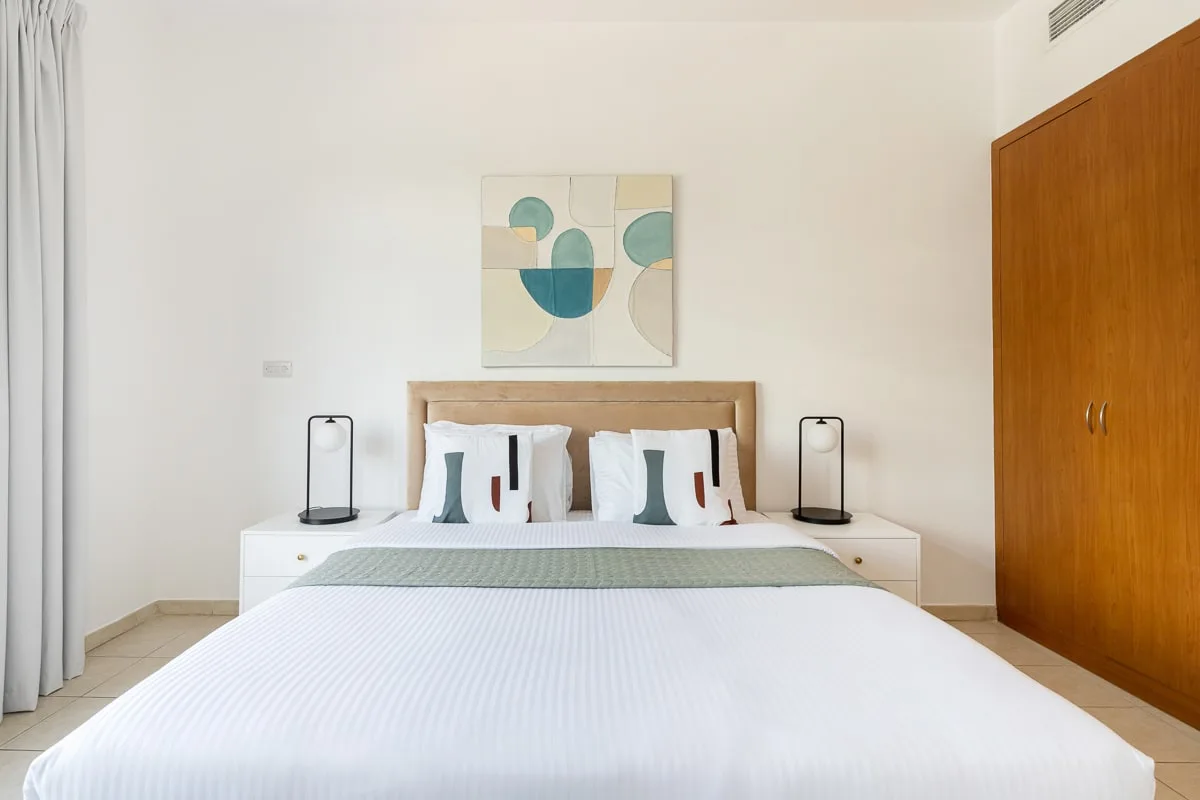 Un dormitorio luminoso con una cama bien tendida y arte abstracto sobre el cabecero.