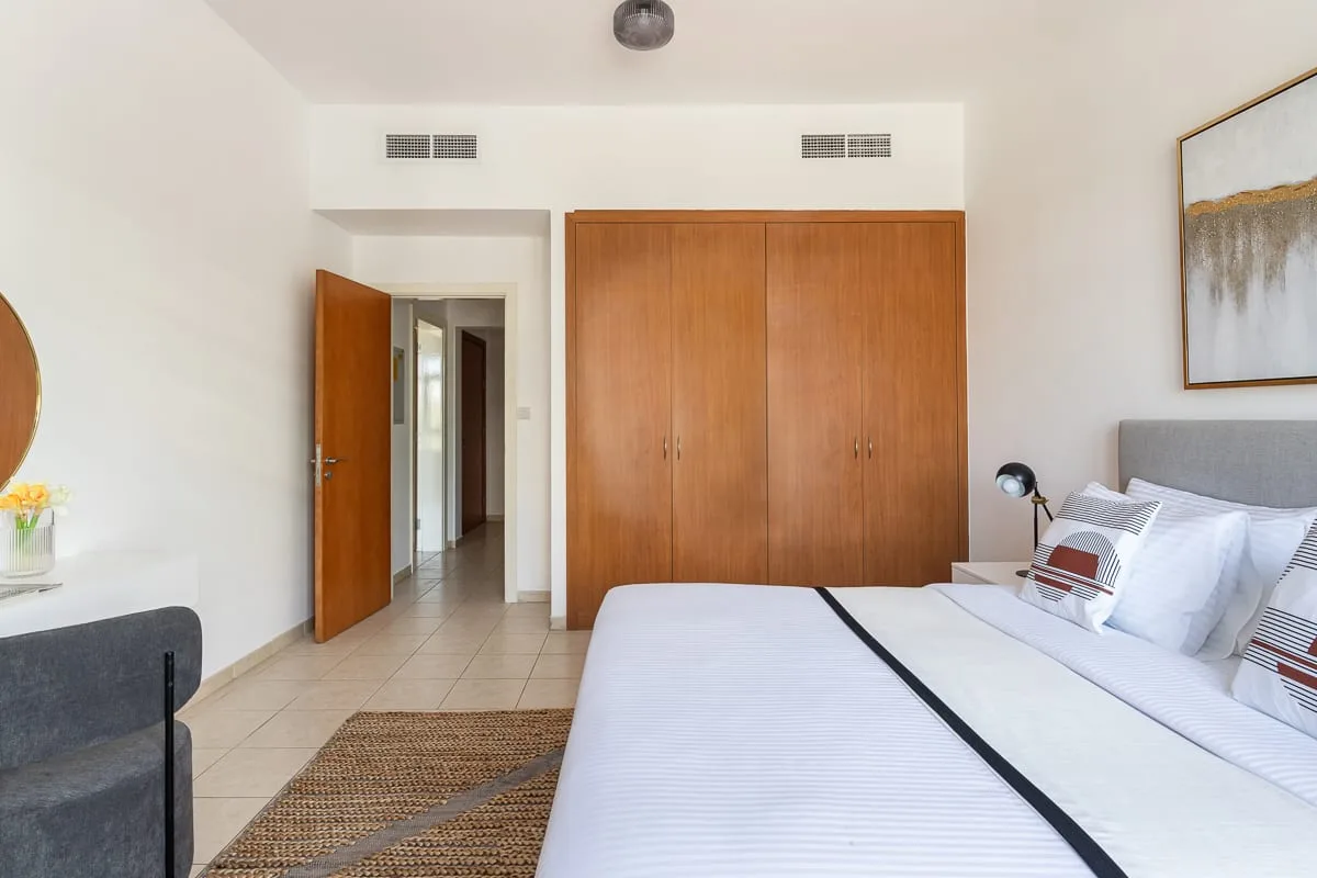 Un dormitorio luminoso con una cama bien tendida y un armario de madera.