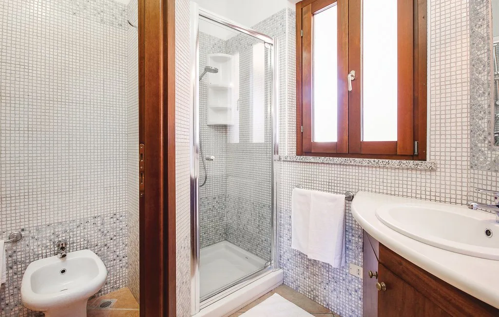 A tiled bathroom with a glass shower, sink, and window.