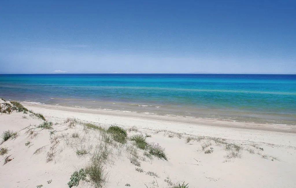 A sandy beach with sparse dune grass overlooks the blue sea.