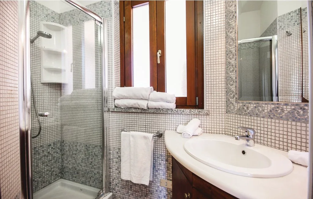 A tiled bathroom with a glass shower, sink, and mirror.
