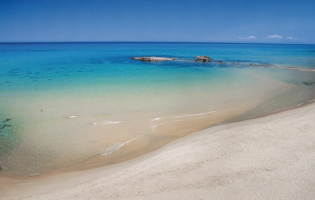 A sandy beach meets clear turquoise water beneath a blue sky.