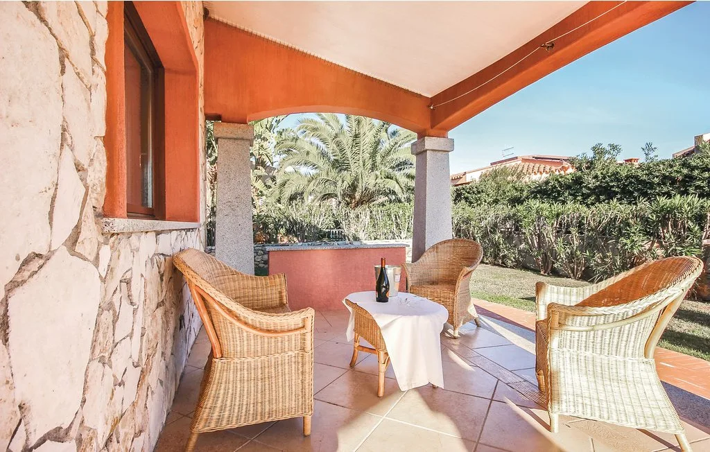 A covered patio with wicker seating around a small table overlooks a garden.