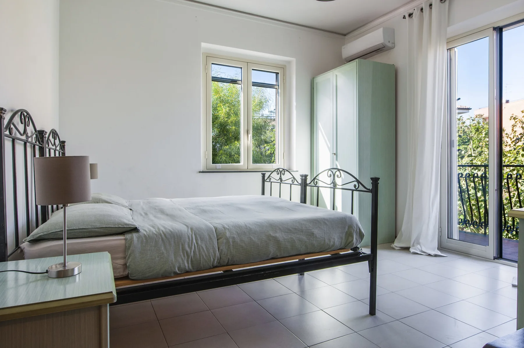 A bright bedroom with a bed, a wardrobe, and glass doors opening onto a balcony.