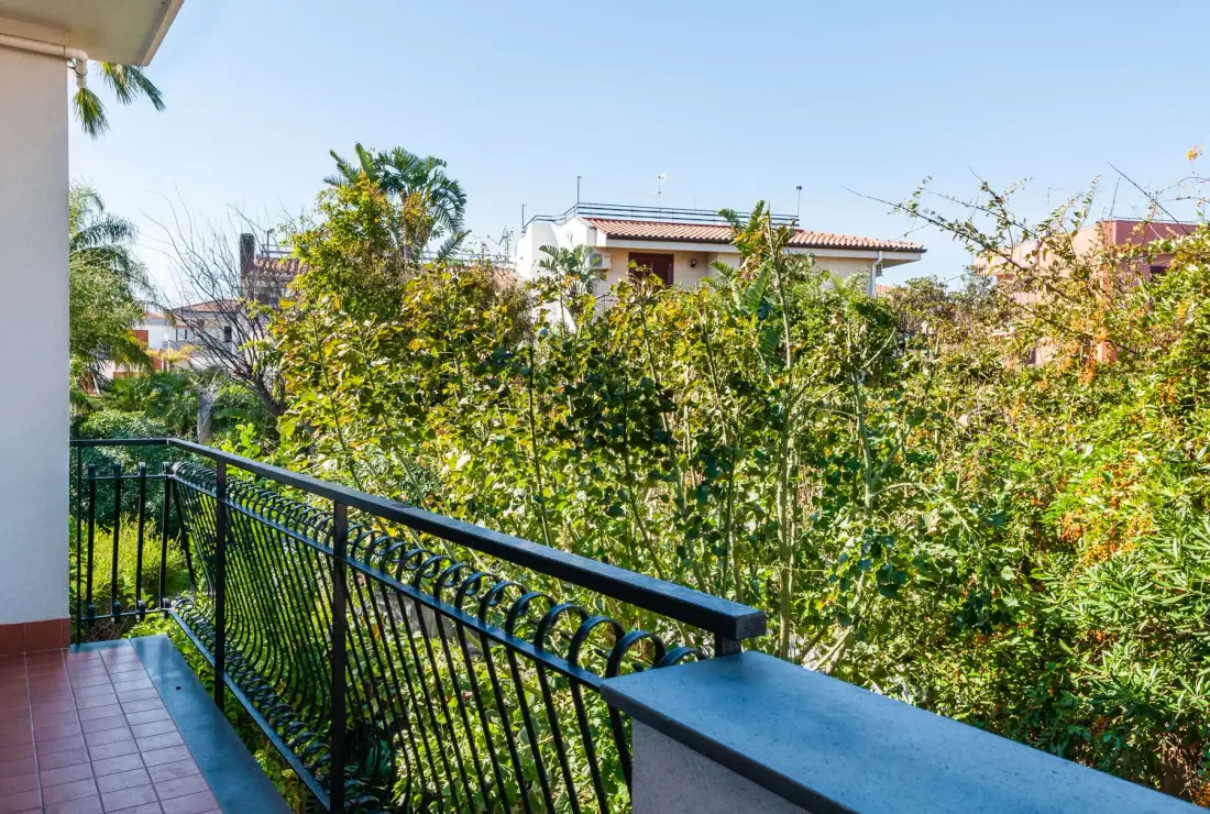 A balcony overlooks dense greenery and neighboring buildings.
