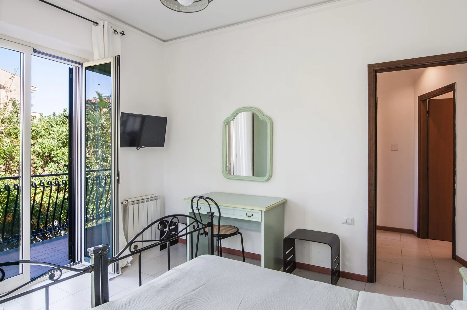A bedroom with a bed, a small vanity, and open balcony doors.