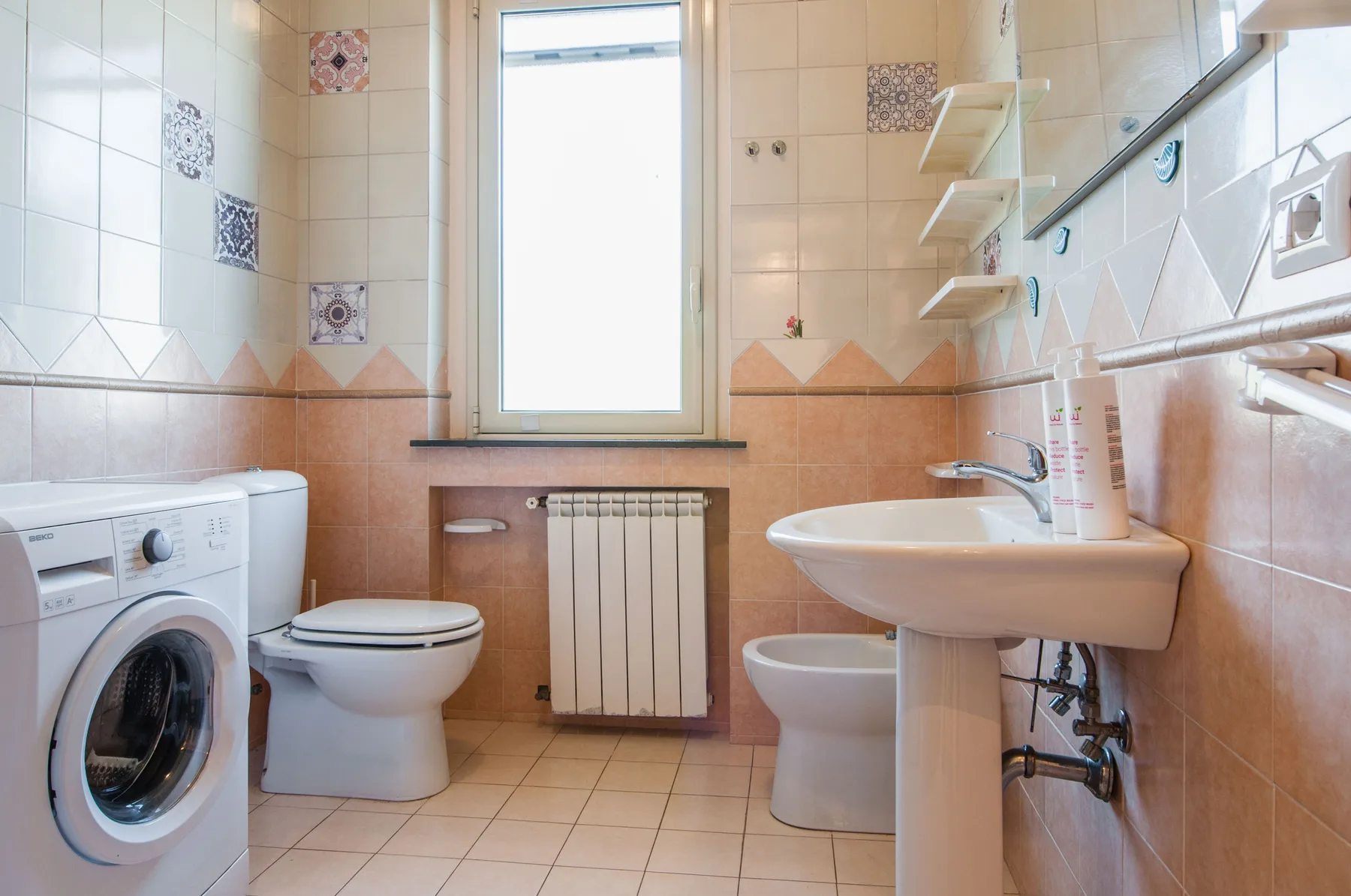 A tiled bathroom with a washing machine, toilet, sink, and window.