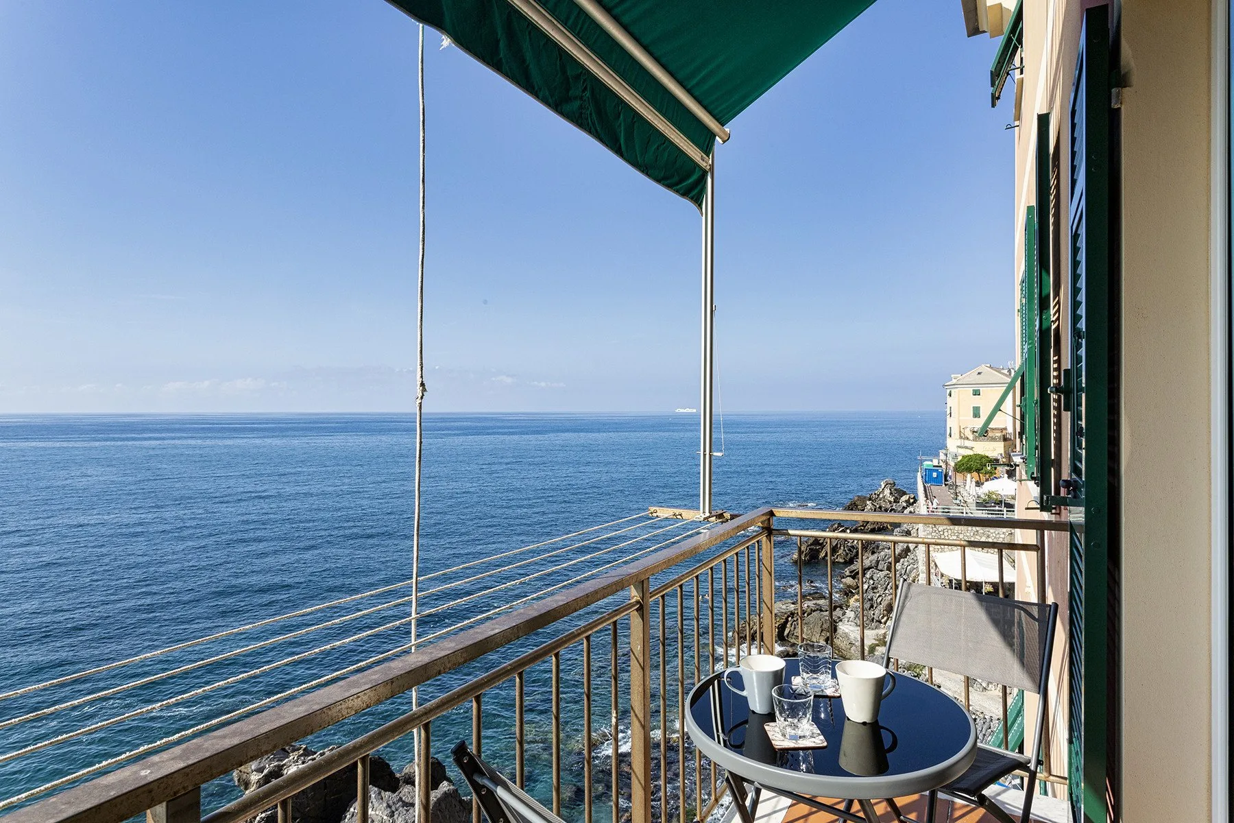 A balcony overlooks the sea, with a small table beneath a green awning.