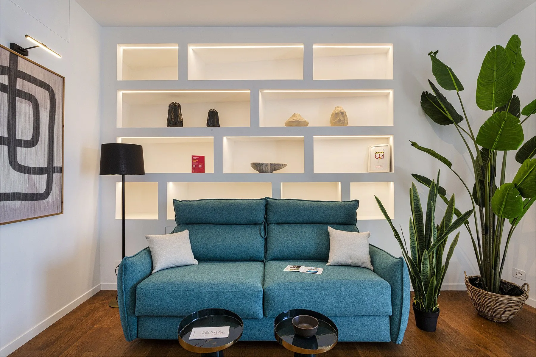 Una sala de estar con asientos azules, estantes iluminados y plantas de hojas grandes.