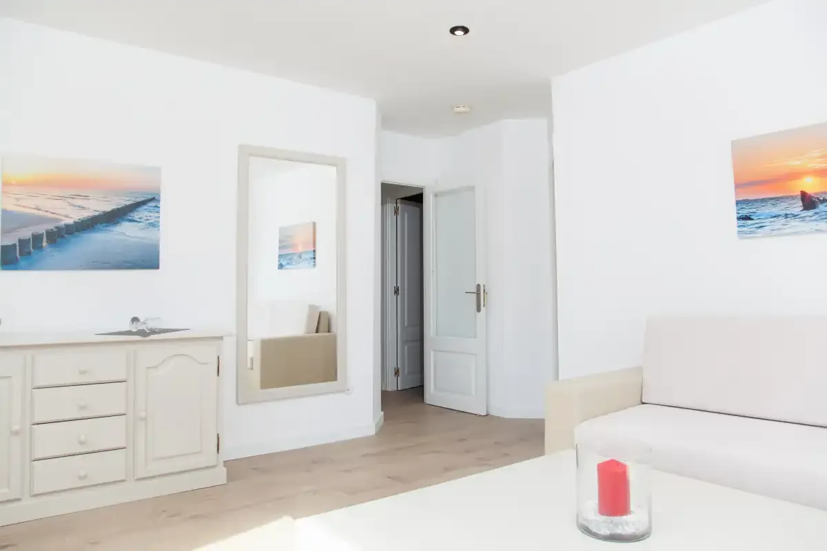 Una sala de estar luminosa con asientos blancos e imágenes enmarcadas del mar.