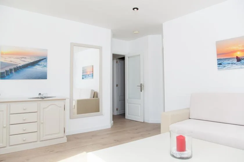 Un dormitorio luminoso con asientos blancos, cuadros costeros y suelo de madera clara.