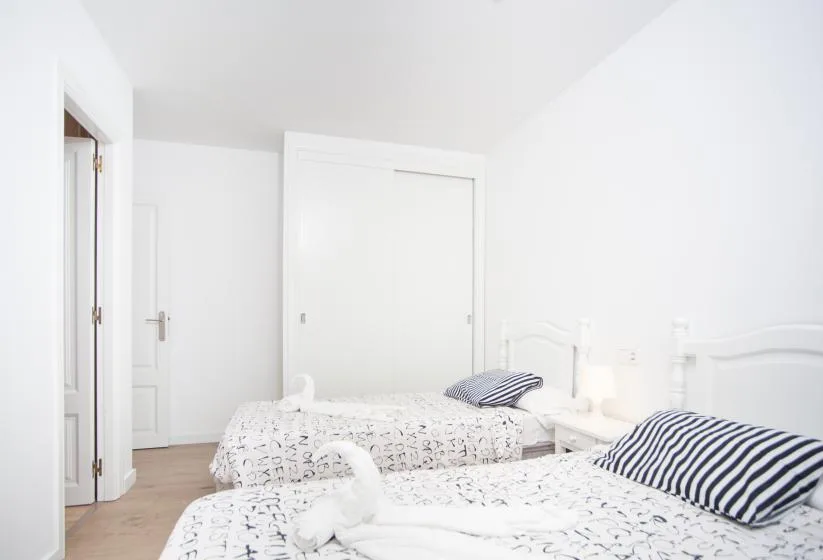 Un dormitorio luminoso con dos camas vestidas con ropa de cama blanca estampada.