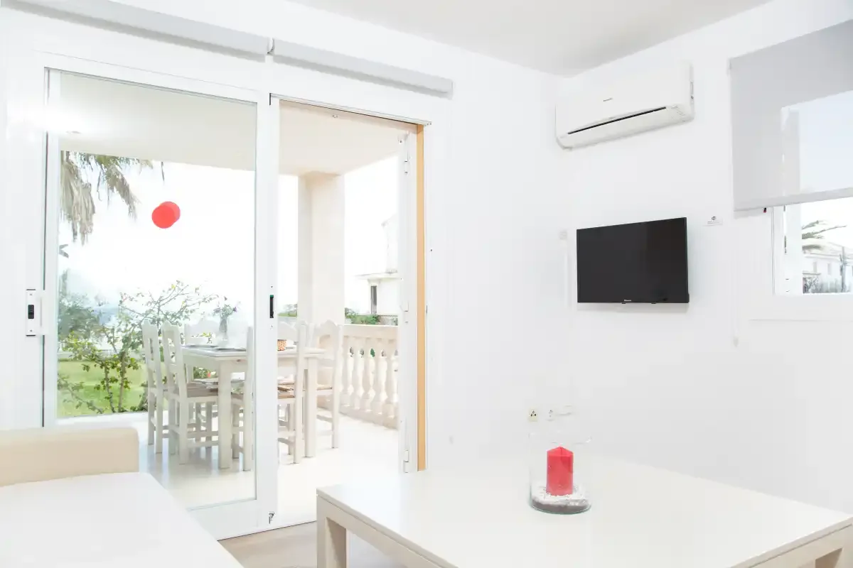 Sala de estar luminosa con una mesa blanca y puertas corredizas de vidrio que dan a un patio.
