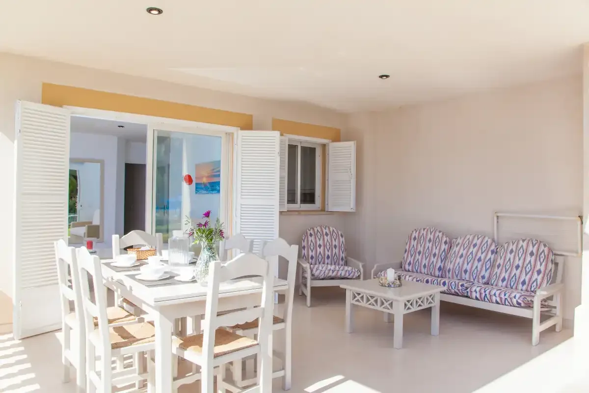 Una luminosa zona de comedor y estar con una mesa blanca y asientos estampados.