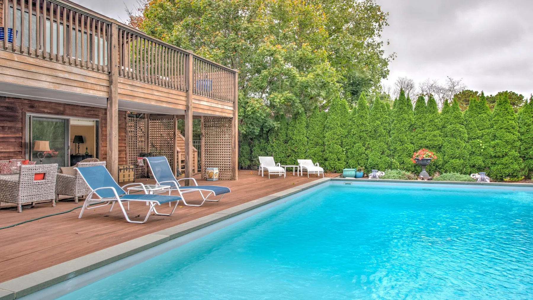 An outdoor swimming pool beside a wooden deck with lounge seating.