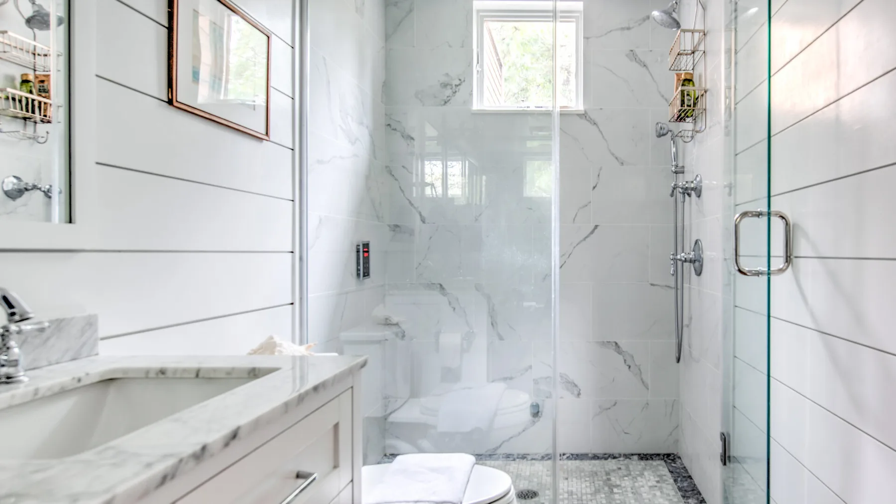 Un baño luminoso con ducha de vidrio y paredes con vetas de mármol.