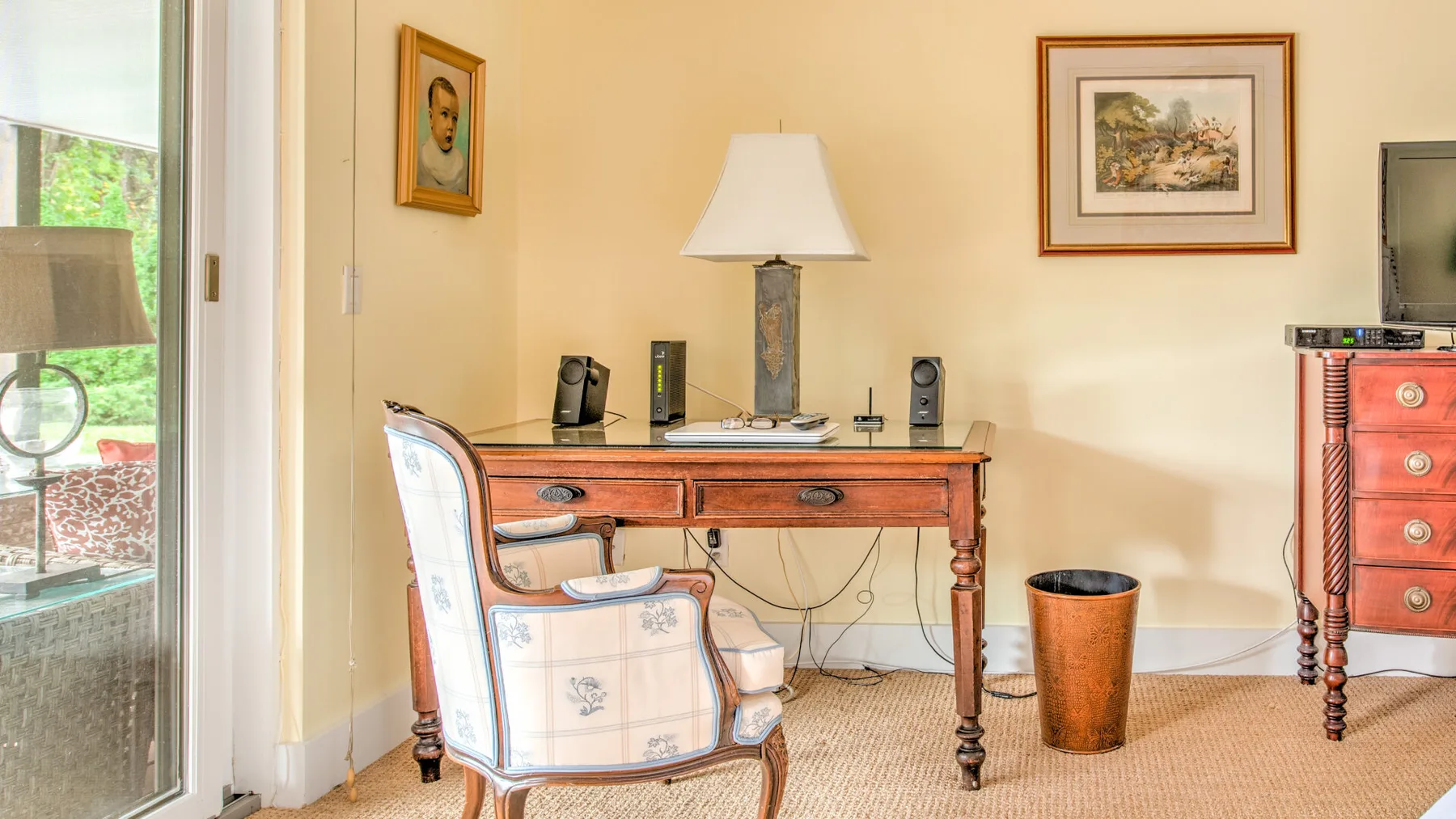 Una habitación amueblada con un escritorio de madera, asiento tapizado y cuadros enmarcados.