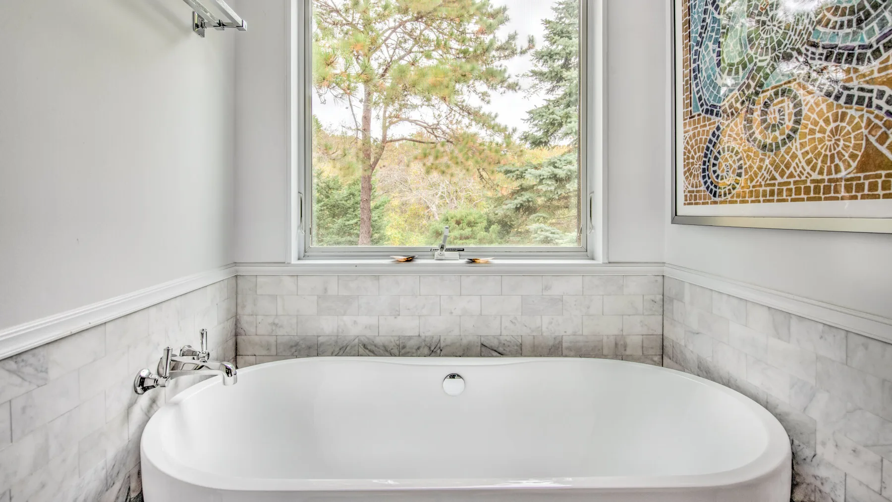 Un baño con una bañera bajo una ventana con vista a los árboles.