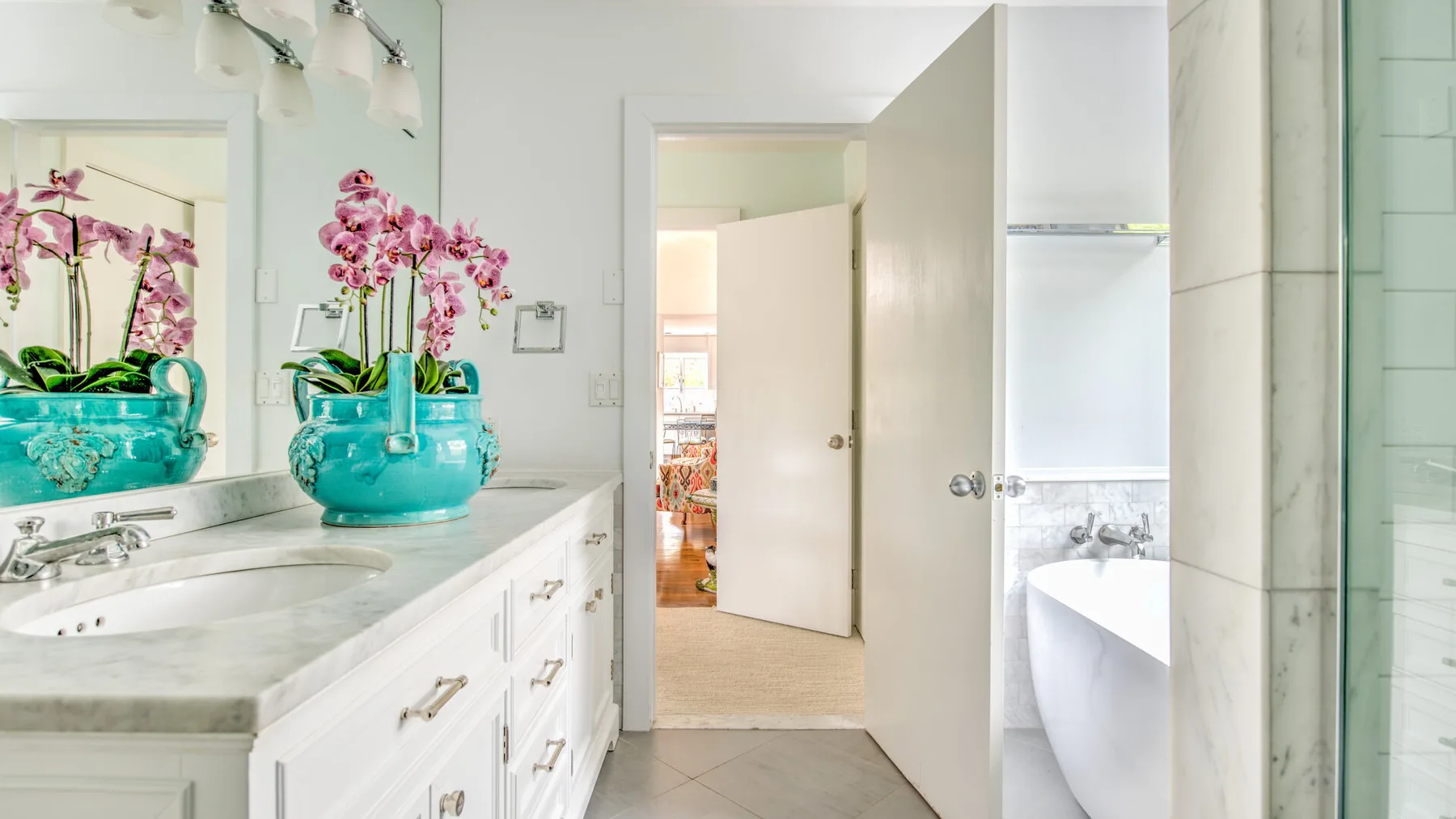 Un baño luminoso con un lavabo blanco, macetas turquesas y una puerta abierta.
