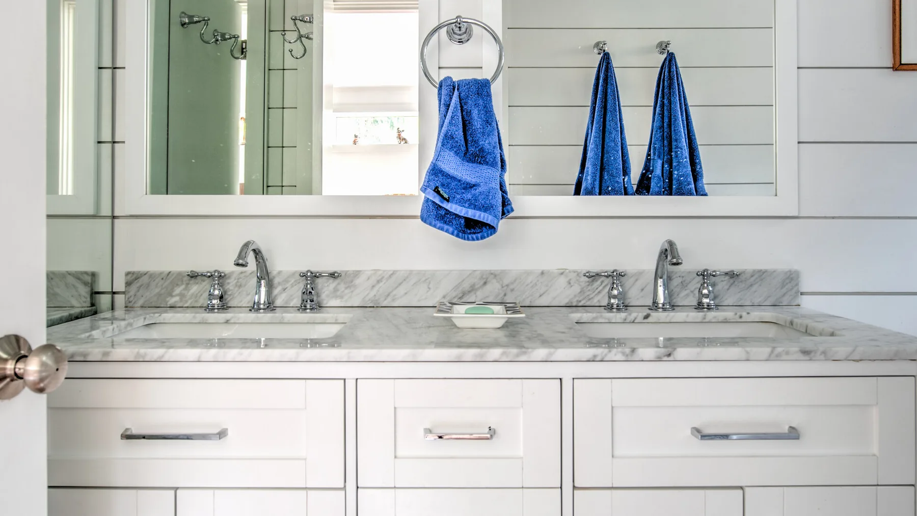 Un tocador de baño con un espejo amplio, una encimera de mármol y toallas azules.