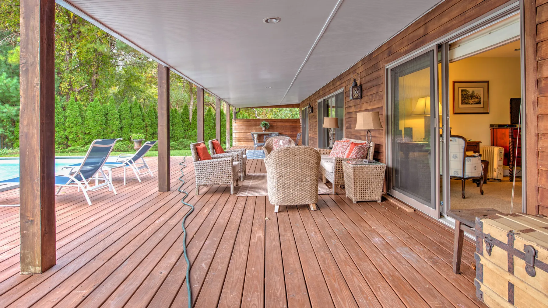 Una terraza cubierta de madera tiene asientos de mimbre junto a una piscina.