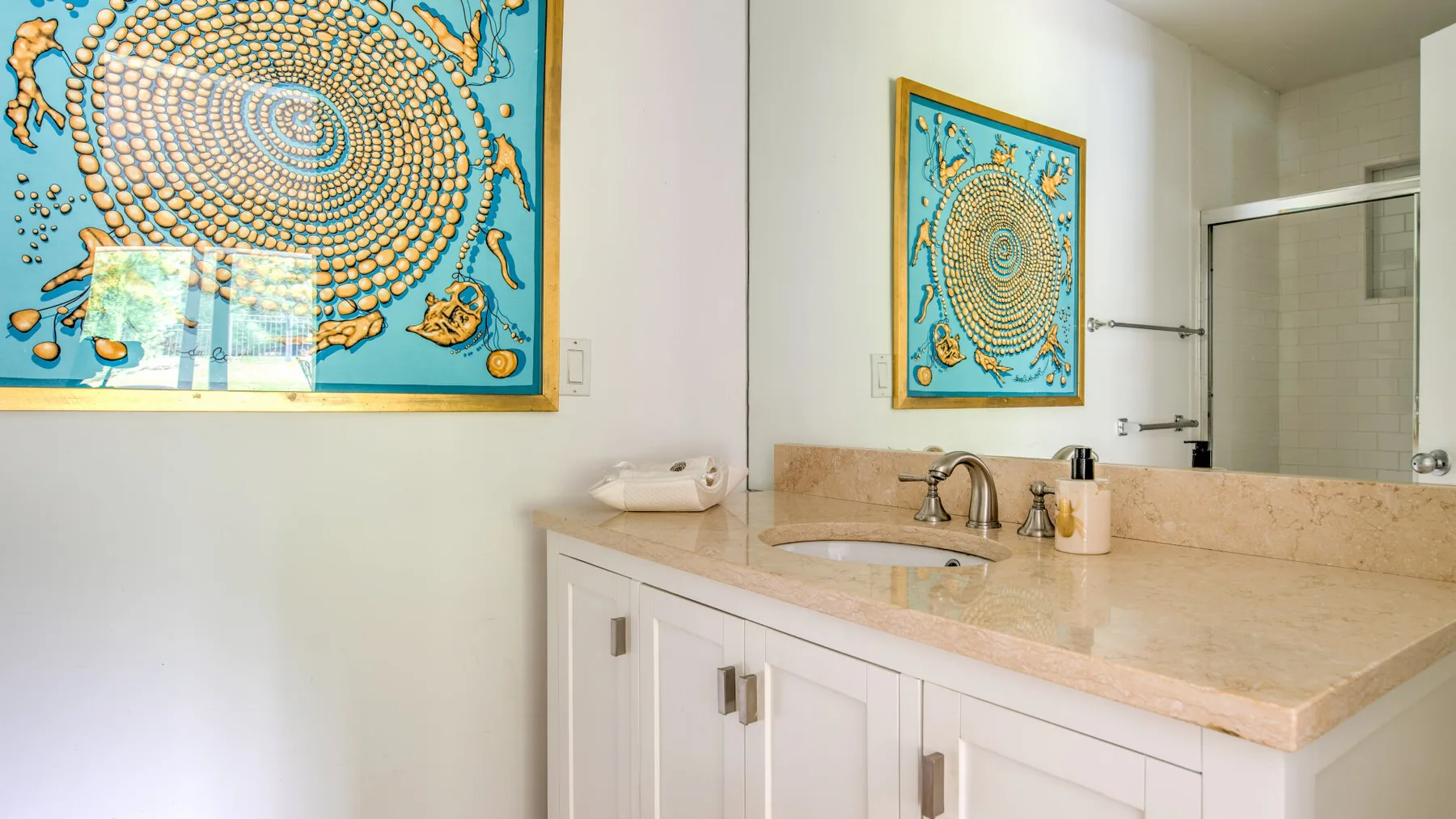 Un tocador de baño luminoso con lavabo, encimera y una colorida obra enmarcada.