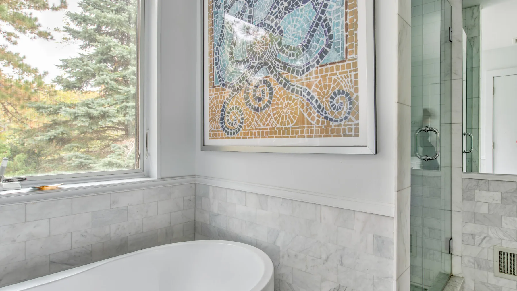 Un baño luminoso con una bañera blanca junto a una ducha de vidrio.