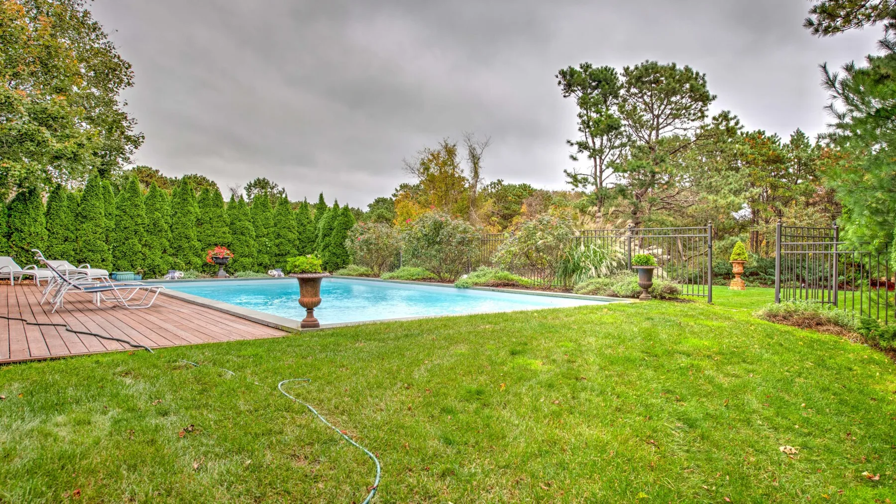 Una piscina al aire libre junto a una terraza de madera y un césped verde.