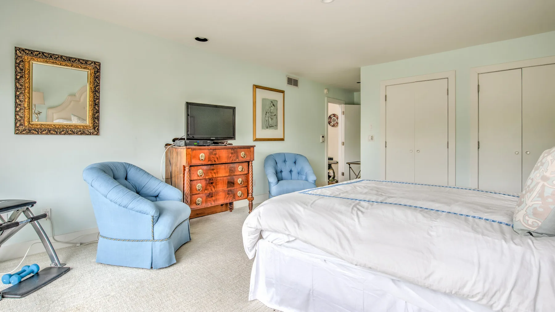 Un dormitorio con una cama, asientos azules y una cómoda de madera.