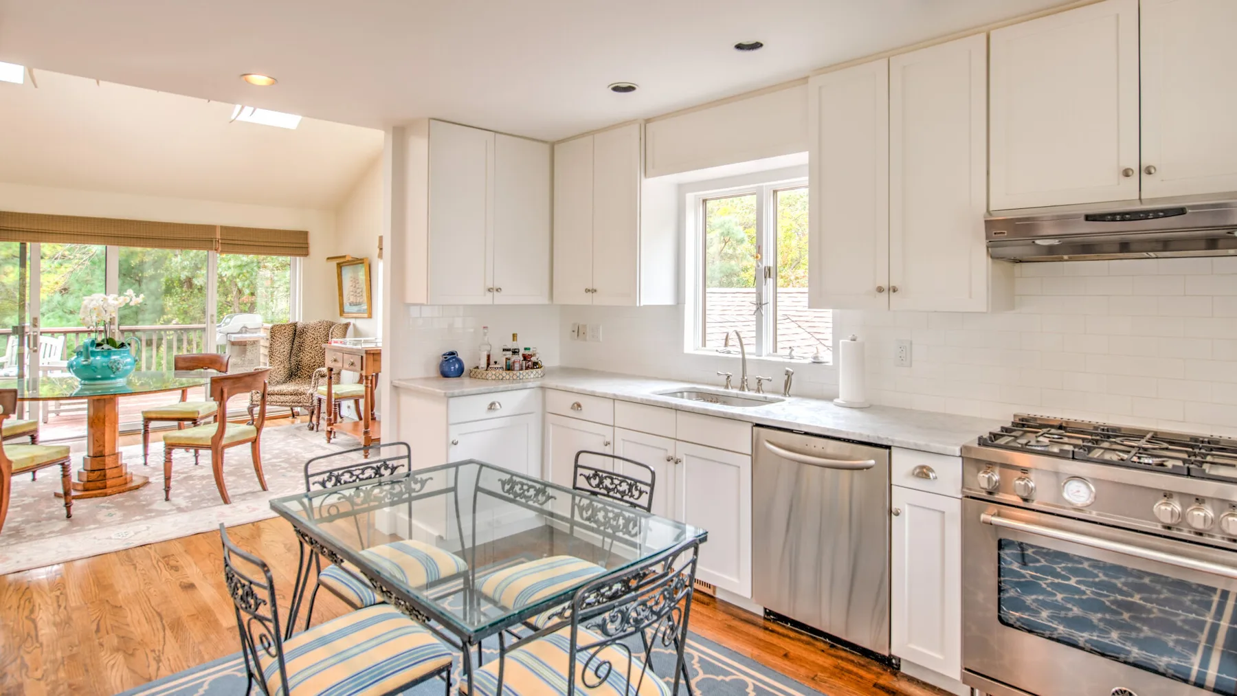 Una cocina luminosa con una mesa de comedor de vidrio y una sala contigua.