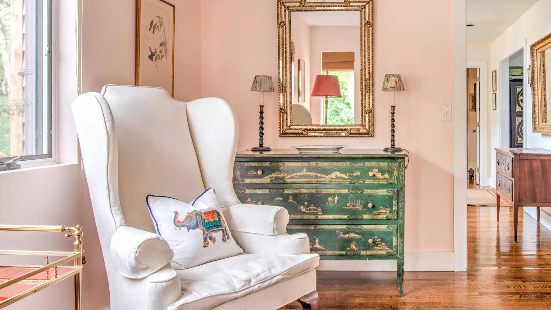 Una zona de estar con un sillón blanco junto a una cómoda verde y un espejo.