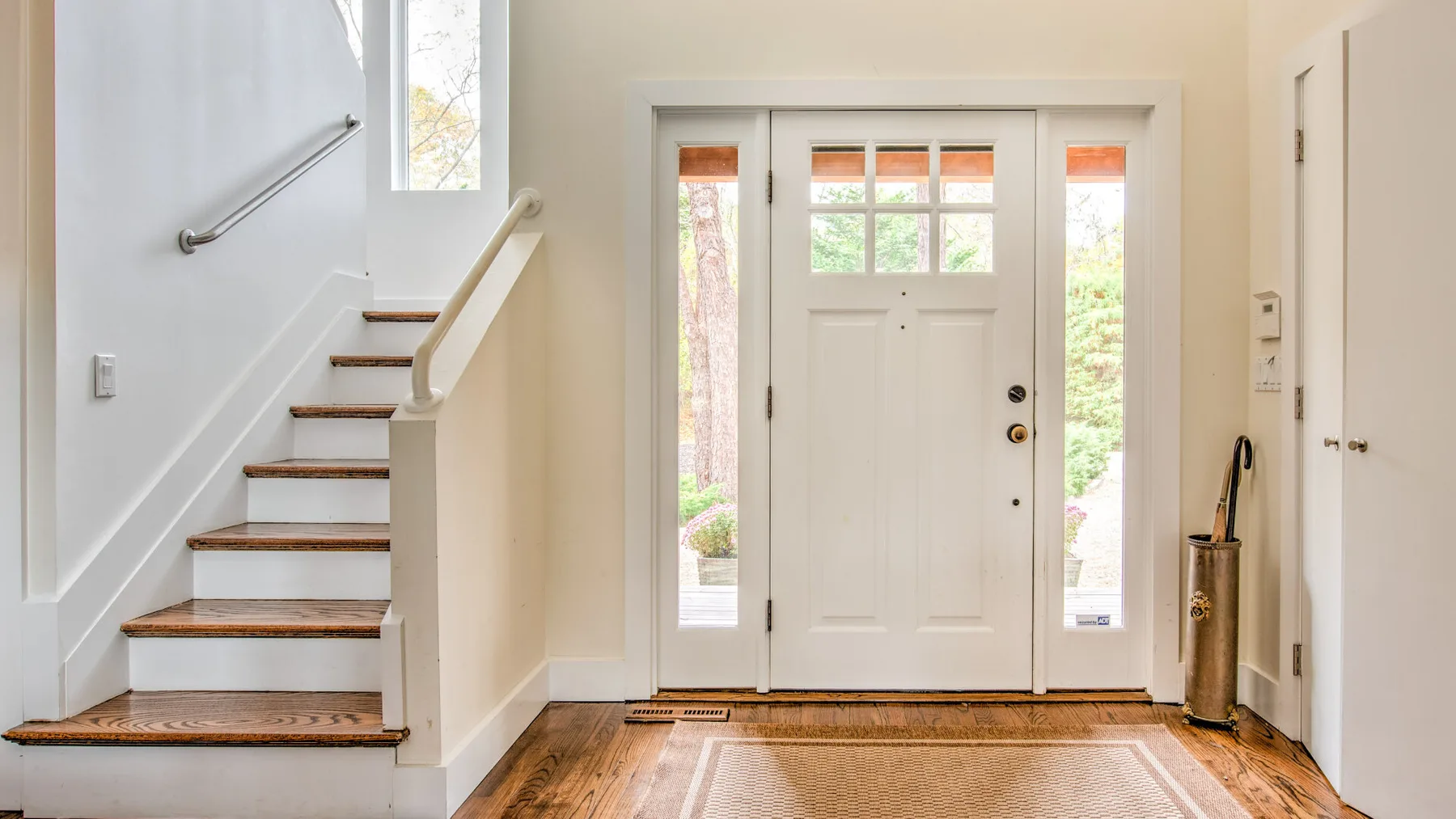 Un recibidor luminoso con una puerta de entrada, ventanas laterales y una escalera.