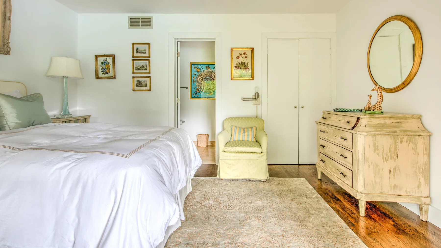 Un dormitorio luminoso con una cama bien tendida y un sillón pequeño.