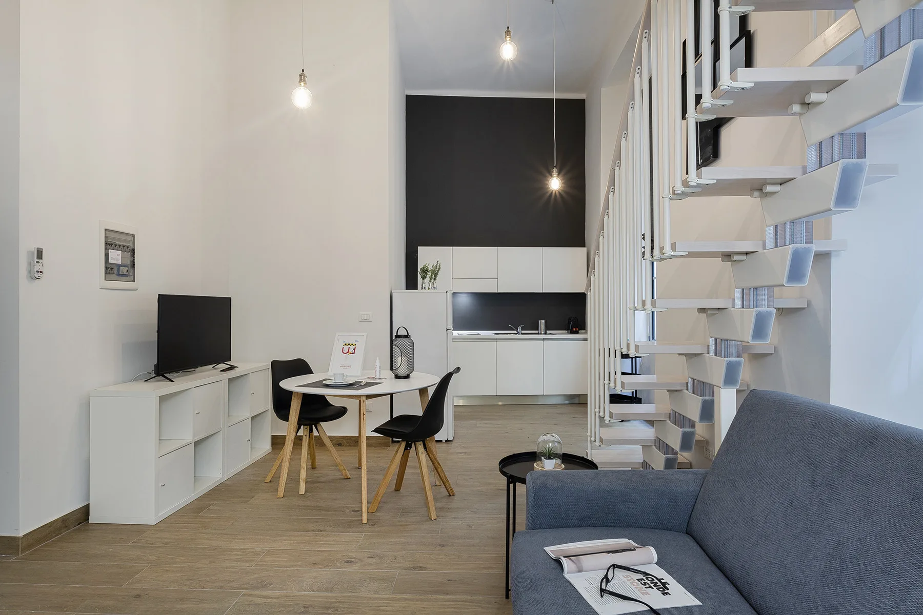 Una zona moderna de estar y comedor con televisor, cocina pequeña y escalera.