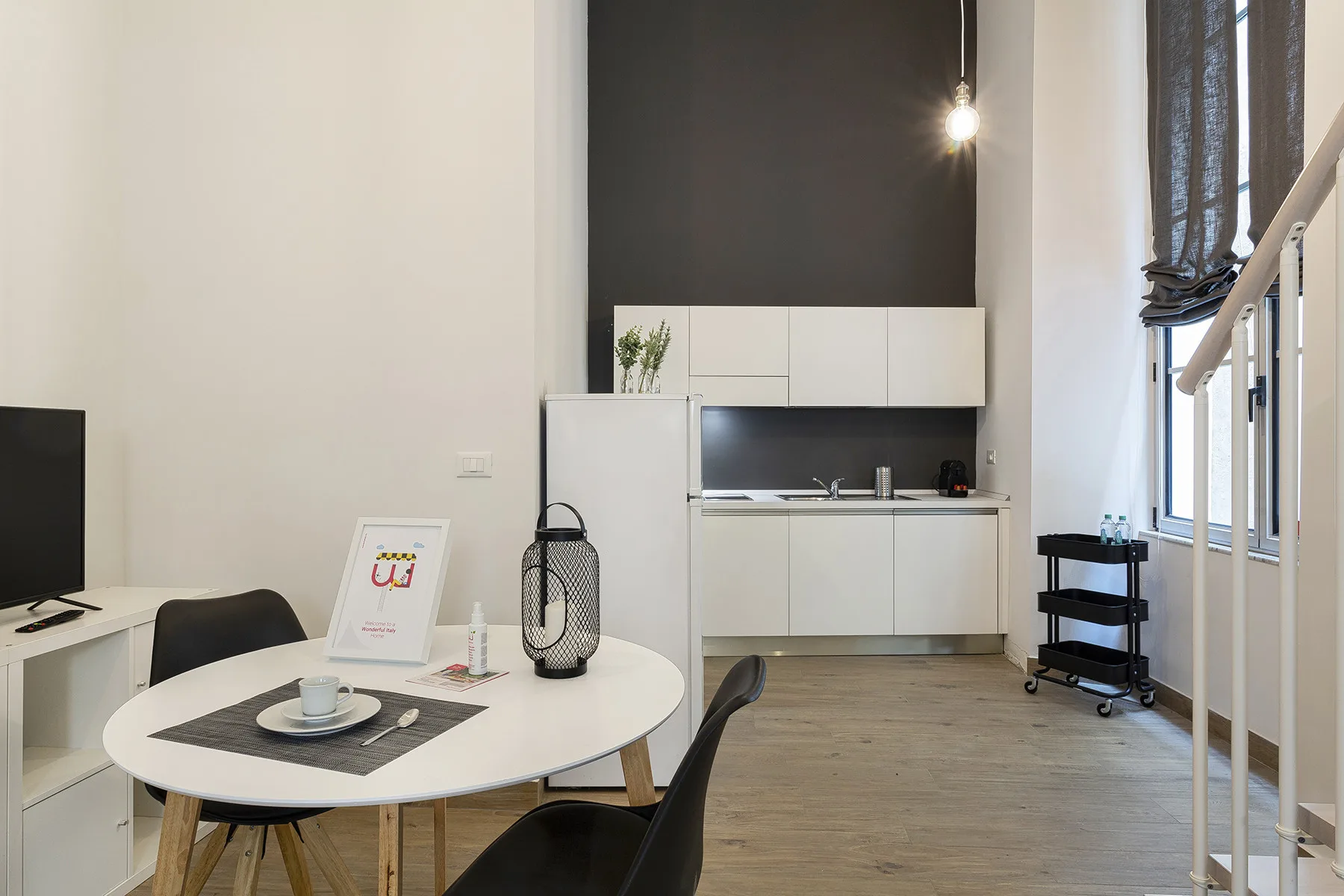 Una estancia luminosa y abierta con cocina pequeña, mesa de comedor y ventanas altas.