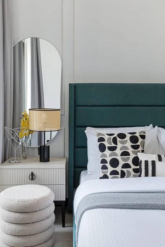 A bedroom with a teal upholstered bed, patterned pillows, and a bedside table.