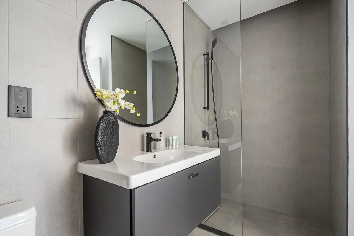 A modern bathroom with a vanity, round mirror, and glass-enclosed shower.