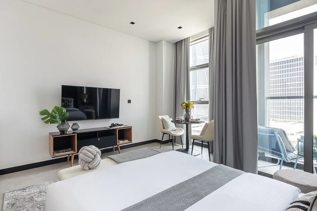 A bright bedroom with a wall-mounted television and floor-to-ceiling windows.