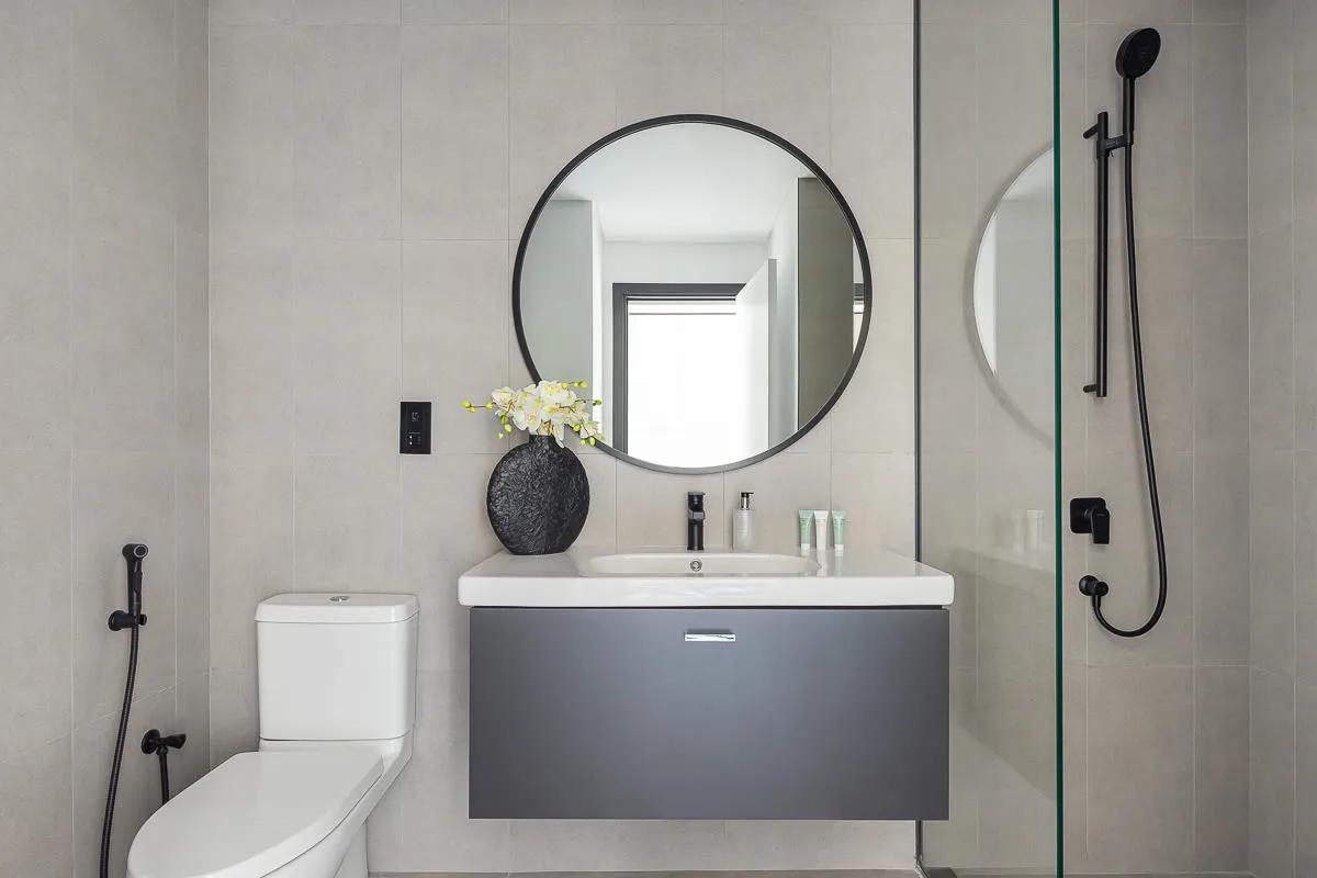 A modern bathroom with a floating vanity, round mirror, toilet, and glass shower.