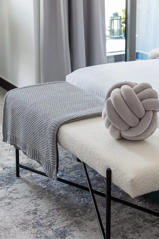 A bedroom with a neatly made bed, textured throw, and decorative knot cushion.