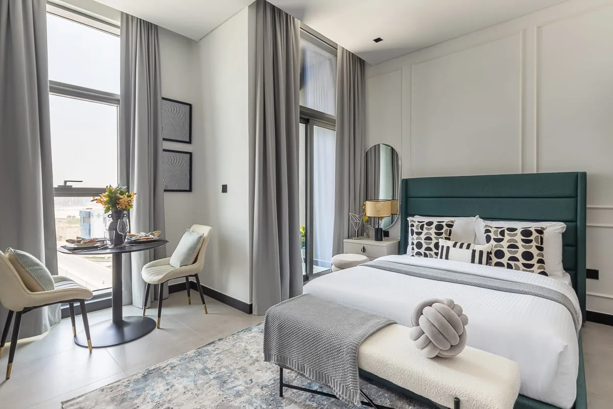 A bright bedroom with a bed, tall windows, and gray curtains.