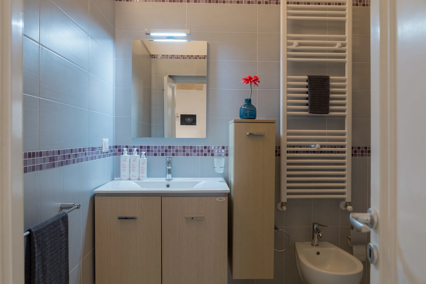 A tiled bathroom with a vanity, mirror, and towel radiator.