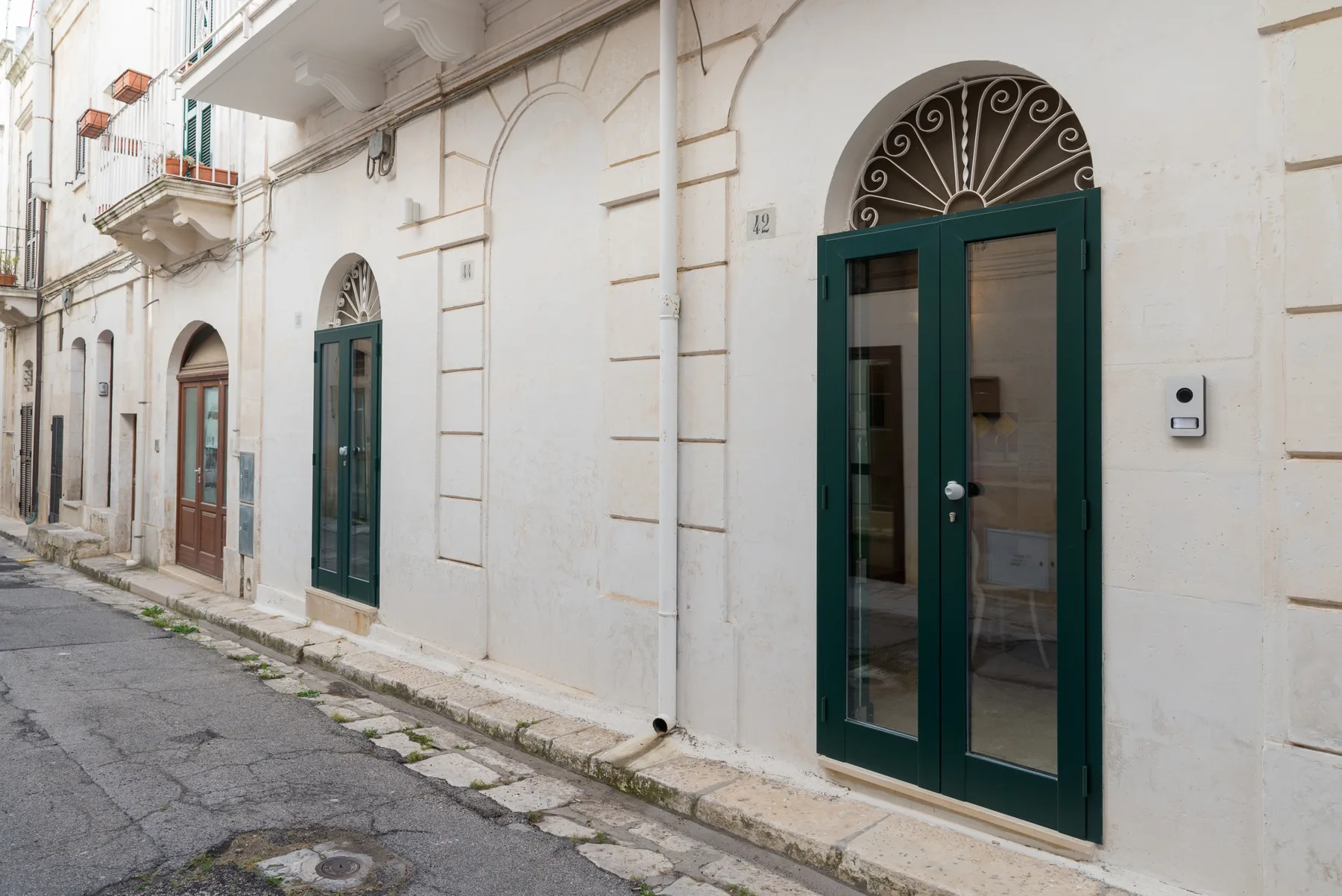A narrow street runs beside a pale building with dark green doors.